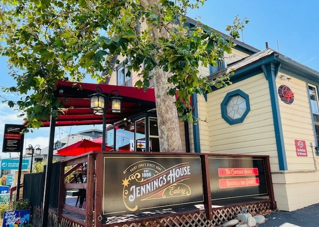 Jennings House exterior: cream siding, blue-green octagonal window trim, café sign and red patio umbrellas
